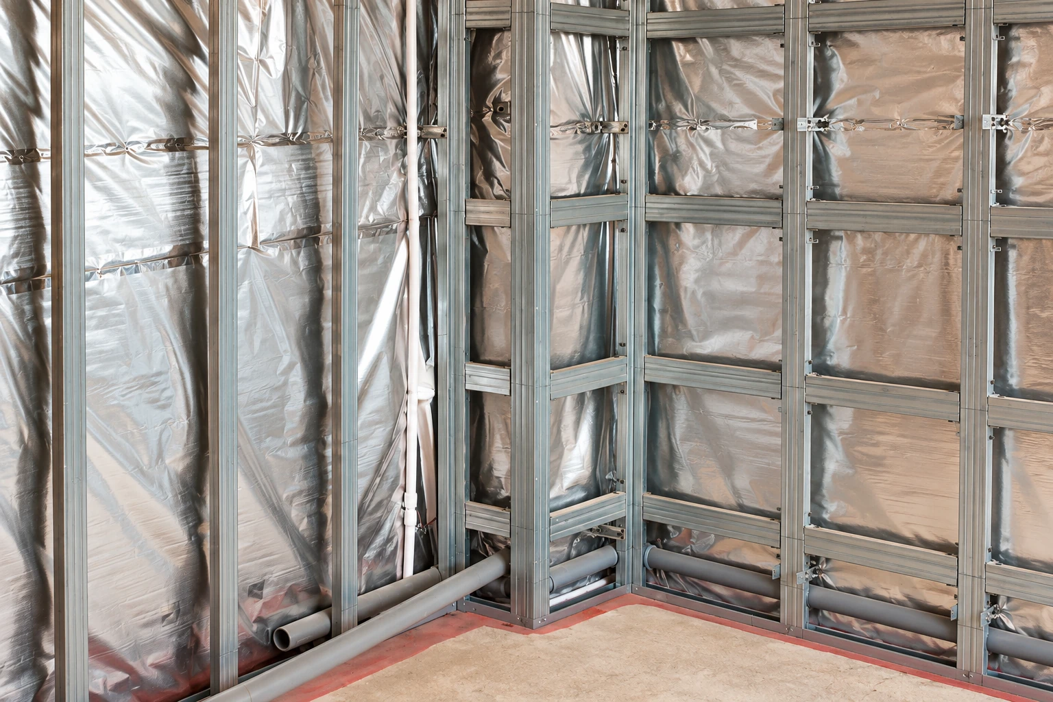 Silver reflective sheeting fills the spaces behind a grid of metal wall studs in an unfinished interior.