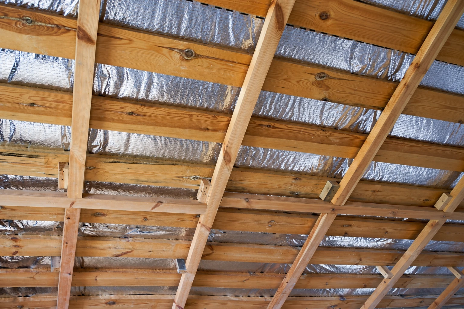 Reflective foil vapor barrier fitted between exposed wooden rafters and joists.